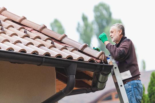 Man on later inspecting tile roof